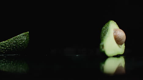 Ripe-green-avocados-are-falling-on-the-glass-with-splashes-of-water-in-slow-motion-on-a-dark-background